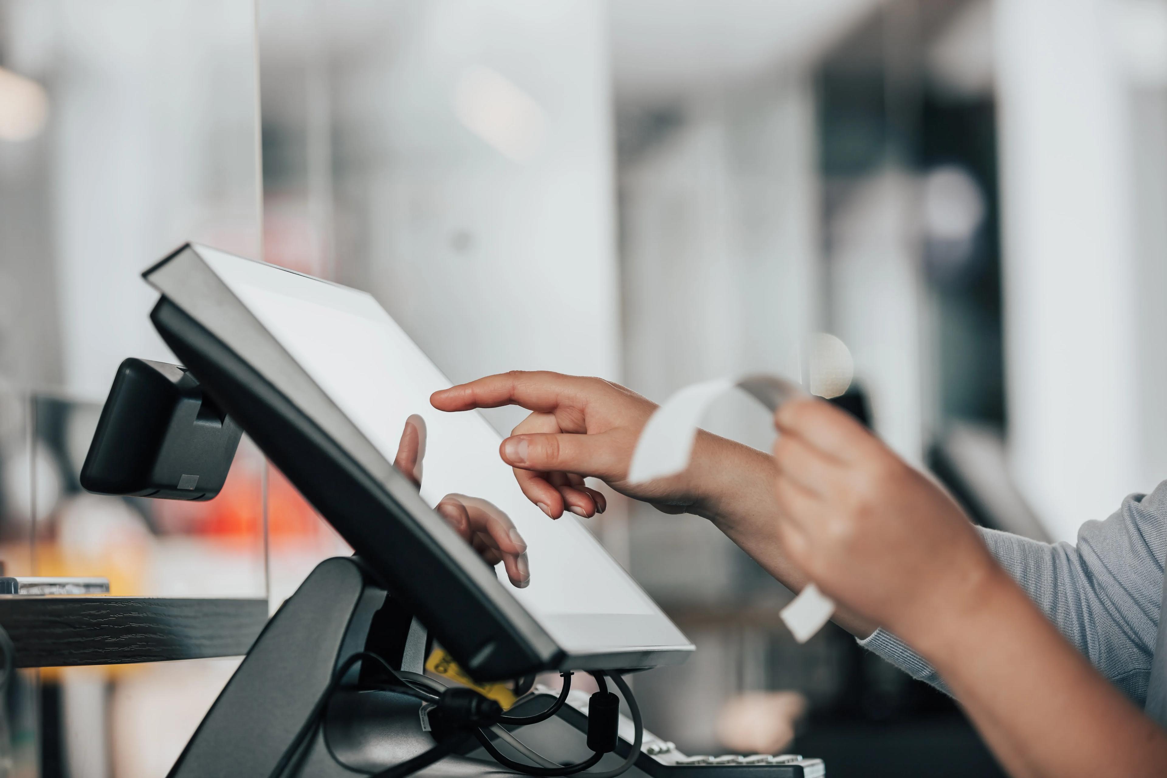 A person's hands hold a paper bill while typing on a POS screen.