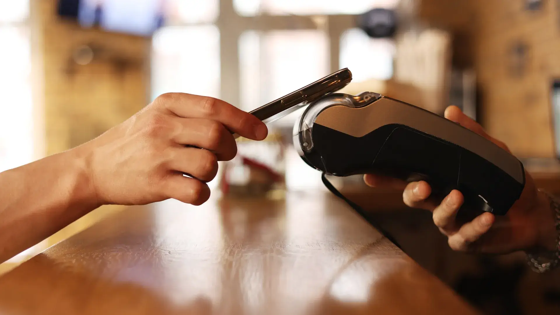 Ein Kunde legt ein Smartphone auf ein mobiles Zahlungsgerät, um kontaktlos zu bezahlen und einen digitalen Beleg automatisiert zu erhalten