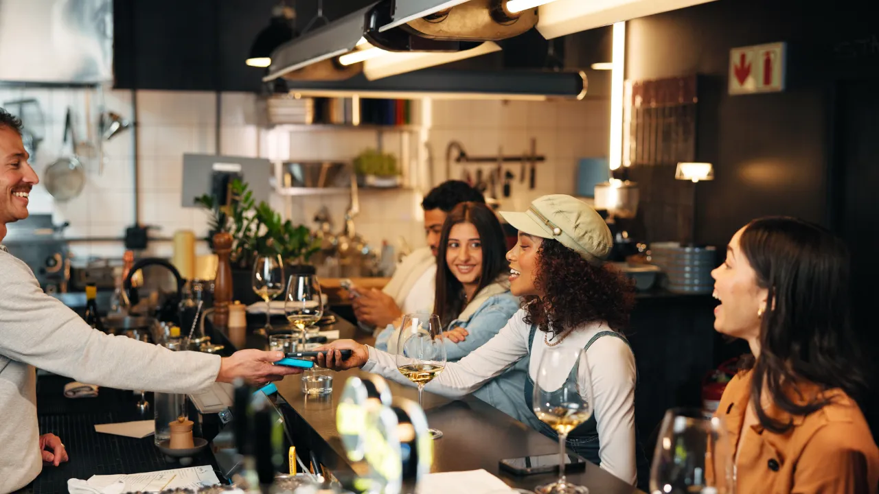 A group of friends at a café counter paying with a mobile phone.