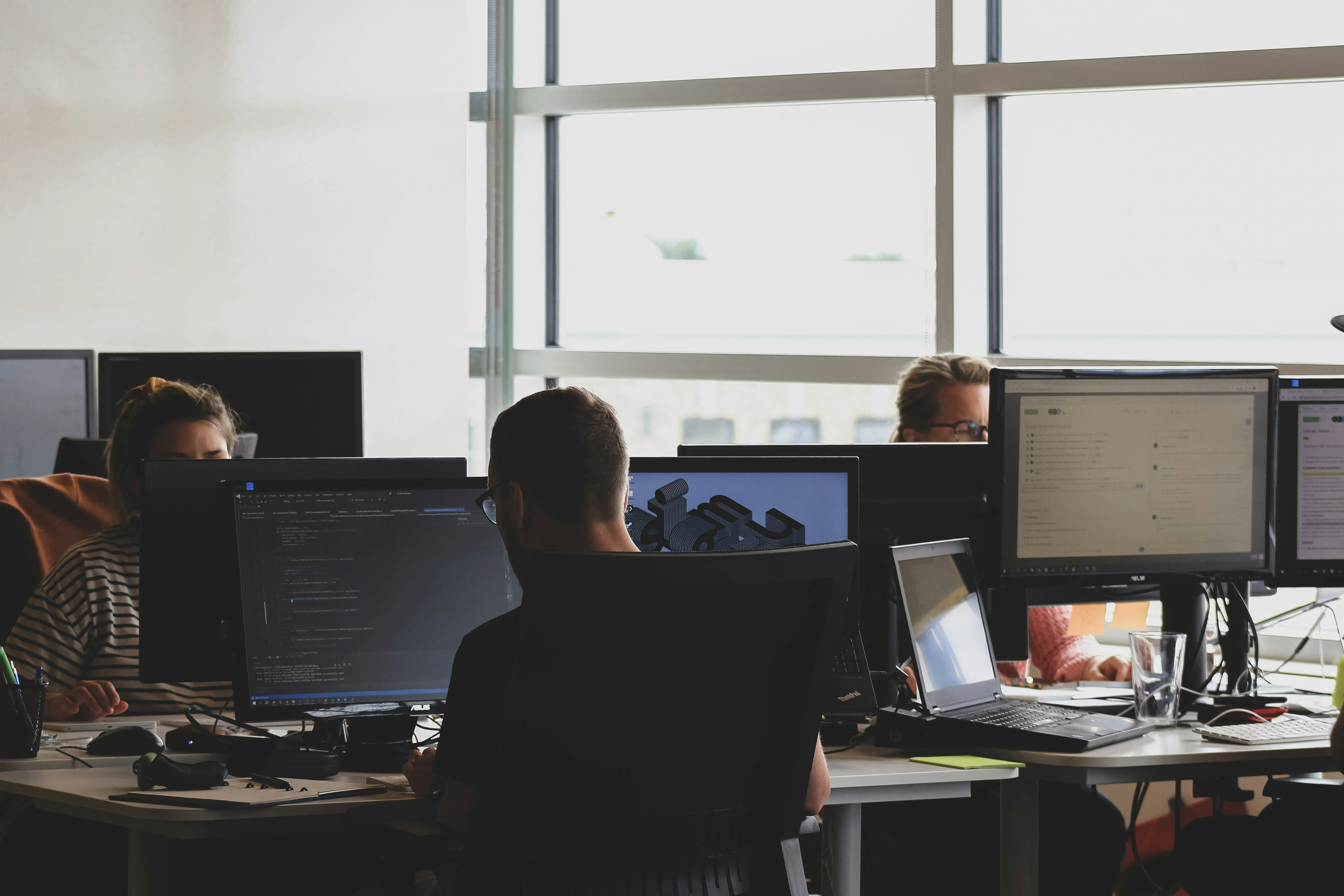 Three people working at desks with computers in an office