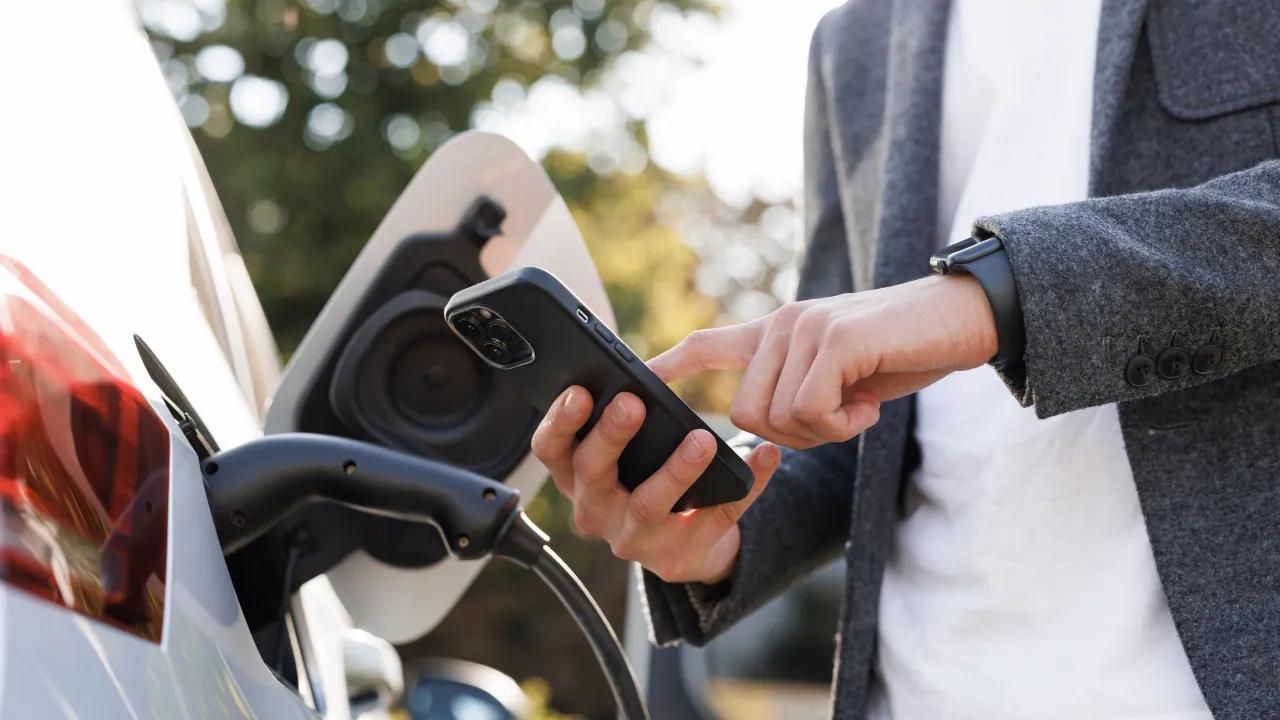 A man operating his smartphone next to the charging electric car